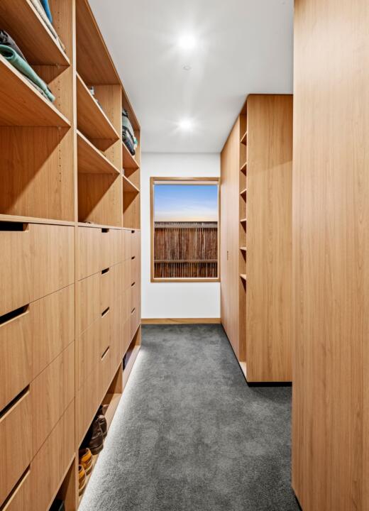 A well lit walk in wardrobe featuring a large glass timber window by Pickering Joinery