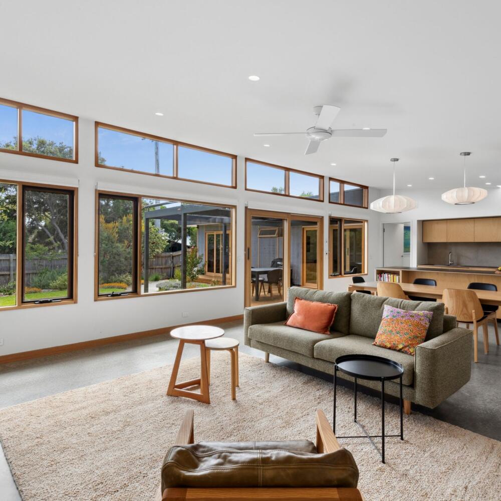 Looking through a living room to the kitchen and beyond into the garden framed by timber windows and doors